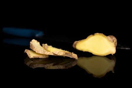 Group of four slices of fresh brown ginger with steel knife isolated on black glass