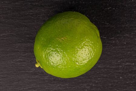 One whole sour green lime flatlay on grey stone