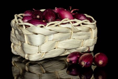 Lot of whole small red onion bulb in bast basket isolated on black glassの写真素材