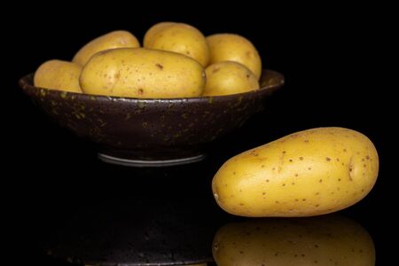 Lot of whole pale yellow potato in dark ceramic bowl isolated on black glassの写真素材
