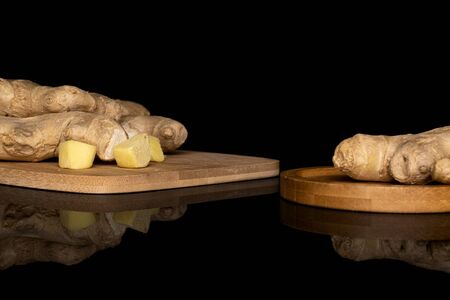 Group of three whole two pieces of fresh brown ginger on bamboo cutting board on round bamboo coaster isolated on black glassの写真素材