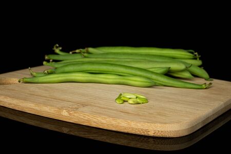 Lot of whole lot of pieces of snap green bean on bamboo cutting board isolated on black glass