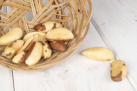 Lot of whole brazil brown nut in round rattan bowl on white woodの写真素材