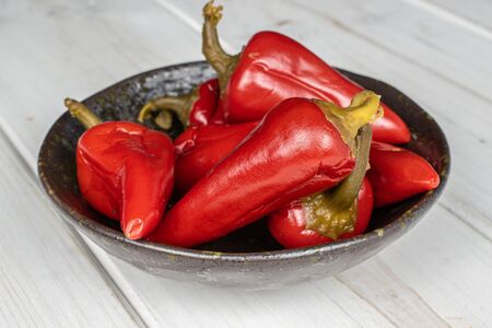 Lot of whole pickled red pepper in glazed bowl on white wood