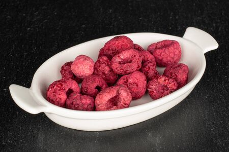Lot of whole dried raspberry on white ceramic plate on grey stone