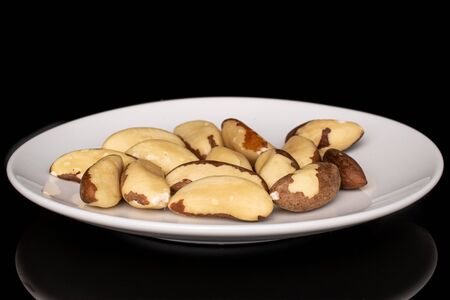 Lot of whole brazil brown nut heap on white ceramic plate isolated on black glassの写真素材
