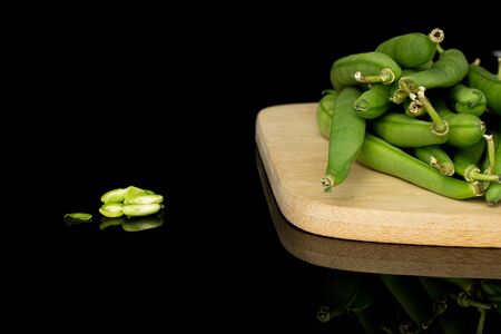 Lot of whole lot of pieces of bright snap green bean on bamboo cutting board isolated on black glass