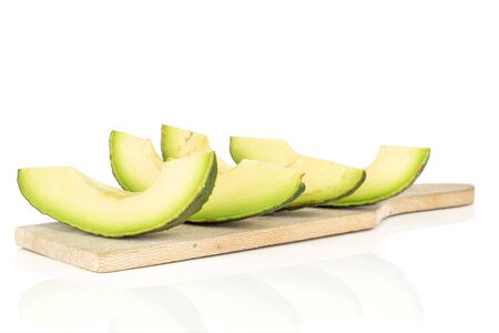 Group of four slices of fresh green avocado on wooden cutting board isolated on white background