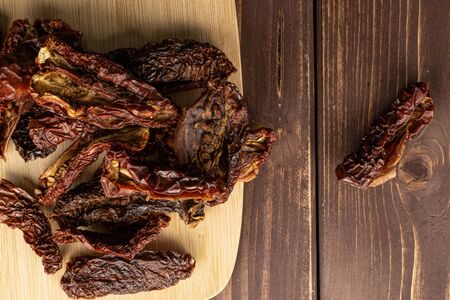 Lot of whole dried red tomato piece on bamboo cutting board flatlay on brown woodの写真素材
