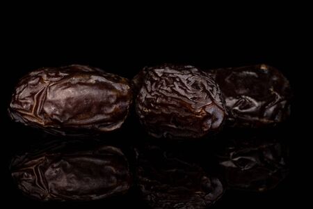 Group of three whole dried brown date fruit isolated on black glass
