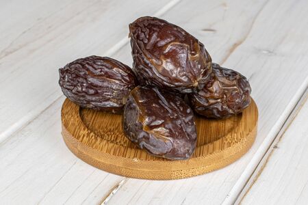 Group of four whole dried brown date fruit on round bamboo coaster on white wood