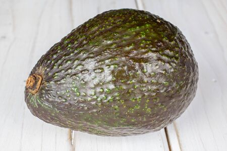 One whole fresh green avocado on white wood