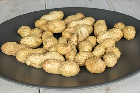 Lot of whole tasty beige peanut on gray ceramic plate on white wood