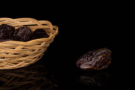 Lot of whole dried brown date fruit in round rattan bowl isolated on black glassの写真素材