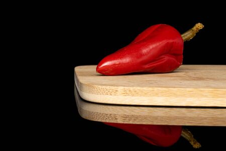 One whole pickled red pepper on bamboo cutting board isolated on black glass