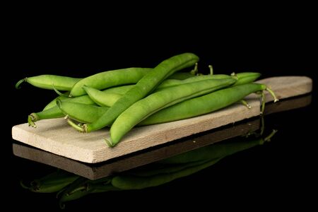 Lot of whole snap green bean on wooden cutting board isolated on black glass