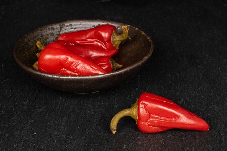 Group of four whole pickled red pepper in glazed bowl on grey stone
