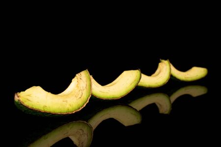 Group of four slices of fresh green avocado isolated on black glass