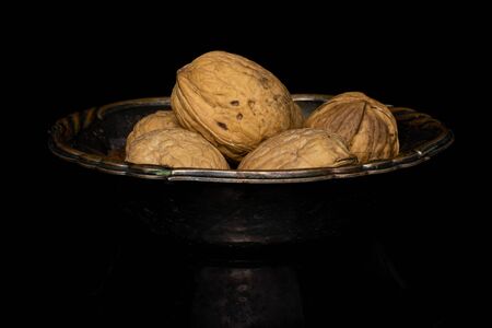Lot of whole tasty brown walnut in glazed bowl isolated on black glass