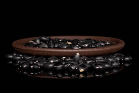 Lot of whole black bean heap with brown ceramic coaster isolated on black glassの写真素材