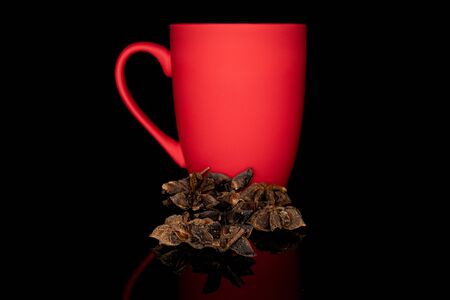 Lot of whole aromatic brown badian with red ceramic cup isolated on black glass