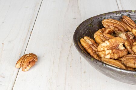 Lot of whole tasty brown pecan half in glazed bowl on white wood