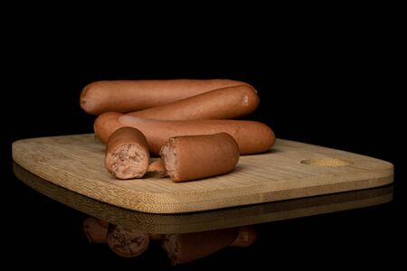 Group of three whole two halves of pork frankfurt sausage on bamboo cutting board isolated on black...