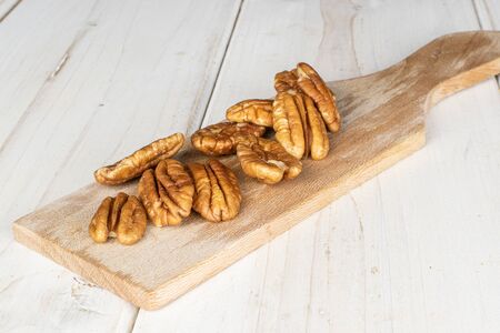 Lot of whole tasty brown pecan half on wooden cutting board on white wood