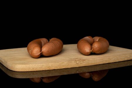 Group of four whole pork frankfurt sausage on bamboo cutting board isolated on black glass