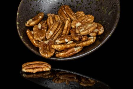 Lot of whole shelled tasty brown pecan half in glazed bowl isolated on black glass