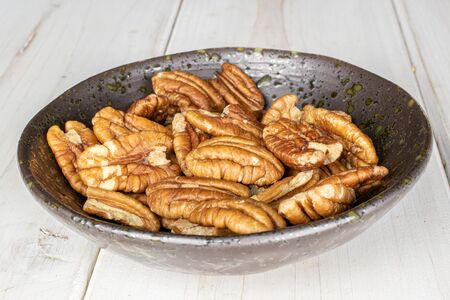 Lot of whole tasty brown pecan half in glazed bowl on white woodの写真素材