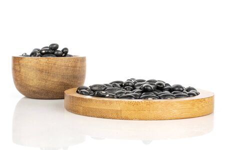 Lot of whole black bean on round bamboo coaster in bamboo bowl isolated on white background