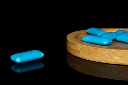 Group of six whole blue chewing gum on round bamboo coaster isolated on black glass