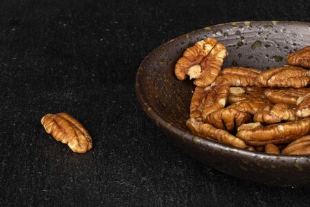 Lot of whole tasty brown pecan half in glazed bowl on grey stone
