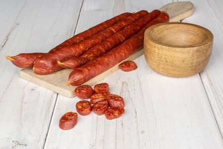 Group of four whole nine slices of piquant smoked sausage in bamboo bowl on wooden cutting board on...