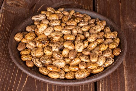 Lot of whole mottled brown bean pinto with brown ceramic coaster on brown wood
