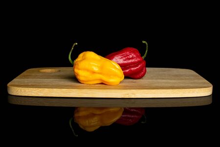Group of two whole hot chili pepper on bamboo cutting board isolated on black glassの写真素材