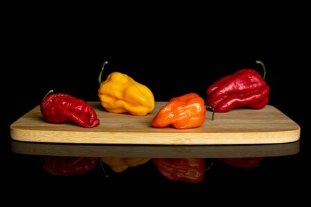 Group of four whole hot chili pepper on bamboo cutting board isolated on black glass
