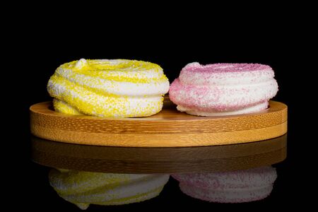 Group of two whole pink and yellow sweet meringue on bamboo coaster isolated on black glassの写真素材