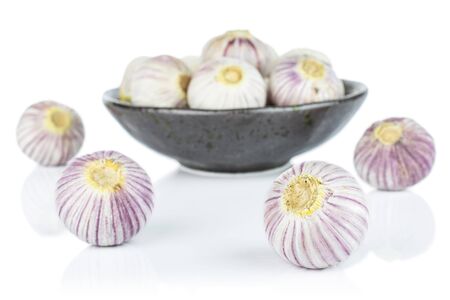 Lot of whole fresh purple single clove garlic in dark ceramic bowl isolated on white backgroundの写真素材