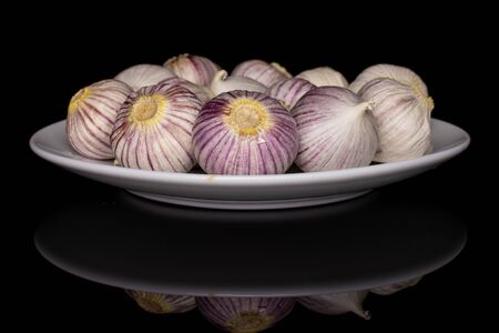 Lot of whole fresh purple single clove garlic on white ceramic plate isolated on black glassの写真素材