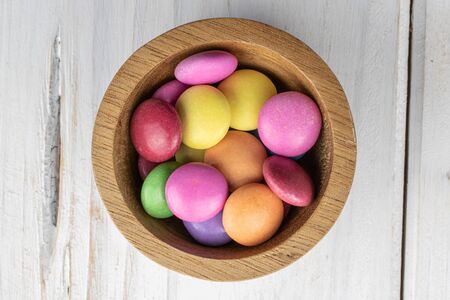 Lot of whole sweet colourful candy in bamboo bowl flatlay on white woodの写真素材