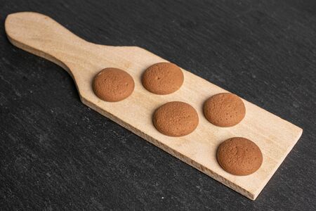 Group of five whole sweet brown chocolate sponge biscuit on small wooden cutting board on grey stoneの写真素材