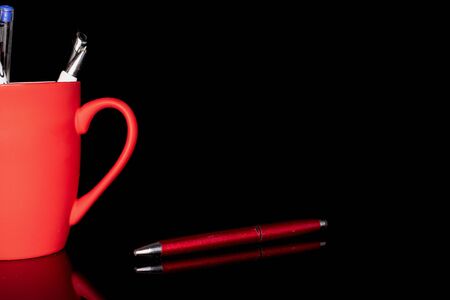 Group of three whole writing ballpoint pen one separated with red ceramic cup isolated on black glassの写真素材