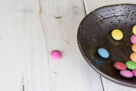 Lot of whole sweet colourful candy in glazed bowl on white woodの写真素材