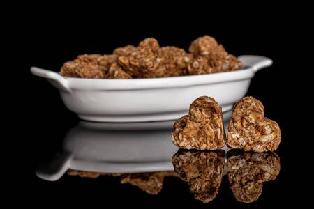 Lot of whole healthy brown cereal heart with cocoa in white oval ceramic bowl isolated on black glassの写真素材