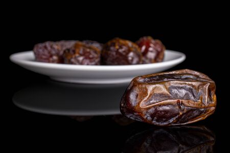 Group of five whole dry brown date fruit on white ceramic plate isolated on black glassの写真素材