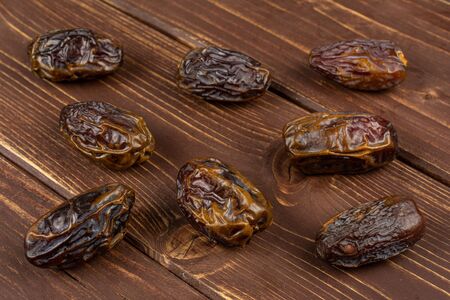 Group of eight whole dry brown date fruit on brown wood