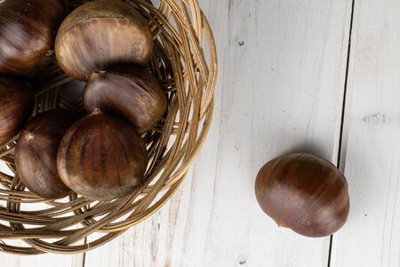 Group of seven whole edible brown chestnut in round rattan bowl flatlay on white woodの写真素材