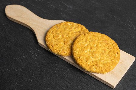 Group of two whole sweet golden oat cookie on small wooden cutting board on grey stoneの写真素材
